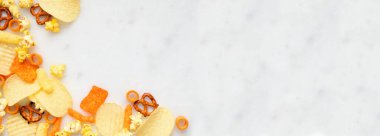 Beyaz mermer afiş üzerinde tuzlu çerezler köşe kenarı. Patates cipsi, patlamış mısır, peynirli börek, kraker. Üst alt görünüm.