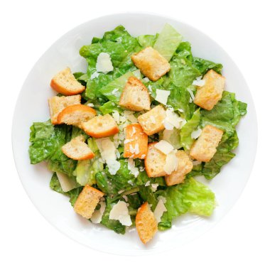 Beyaz arka planda izole edilmiş beyaz bir tabakta geleneksel Sezar salatası, kızarmış ekmek ve parmesan peyniri.