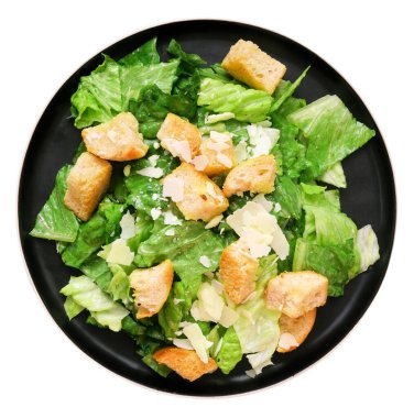 Beyaz arka planda izole edilmiş siyah bir tabakta kızarmış ekmek ve parmesan peynirli klasik Sezar salatası.
