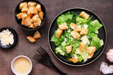 Geleneksel Sezar salatası, kızarmış ekmek ve parmesan peyniri. Üstten alta masa sahnesi koyu arkaplan.