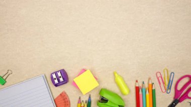 Renkli okul malzemeleri alt sınırdan taşınıyor. Açık kahverengi kağıt arka plan üzerinden yukarıdan aşağıya doğru stop motion loop videosu. Okul konseptine dönelim..