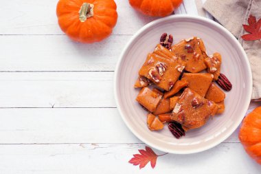 Sonbahar balkabağı, cevizli, kırılgan şeker. Beyaz ahşap bir zemine karşı tabağın üst görüntüsü. Boşluğu kopyala.