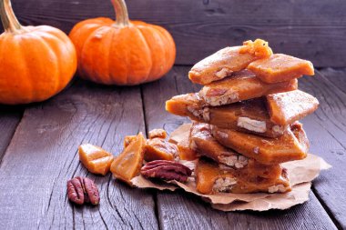 Sonbahar balkabağı pekan cevizli, kırılgan şeker parçaları. Koyu ahşap arka planlı yan manzara.