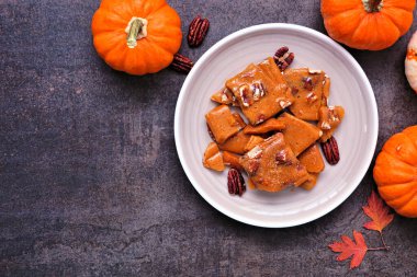 Sonbahar balkabağı, cevizli, kırılgan şeker. Bir tabağın üstünde, koyu renkli bir arka planda. Boşluğu kopyala.