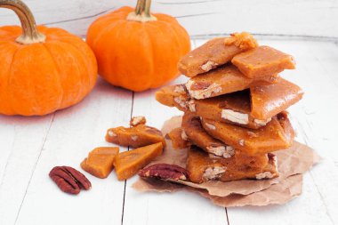 Sonbahar balkabağı, cevizli, kırılgan şeker parçaları yığını. Beyaz ahşap arka planlı yan manzara.