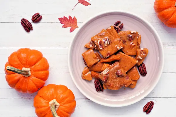 Sonbahar balkabağı, cevizli, kırılgan şeker. Beyaz ahşap arka planda bir plaka üzerinde genel görünüm.