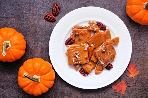 Sonbahar balkabağı, cevizli, kırılgan şeker. Koyu taştan bir zemine karşı tabağın tepesinden aşağı görüş.