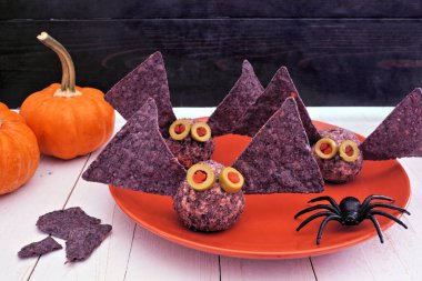 Cadılar Bayramı temalı aperatifler. Mor nacholu yarasa peyniri topları. Kenar görünüm tablosu kırsal bir ahşap zemin üzerine yakın çekim.