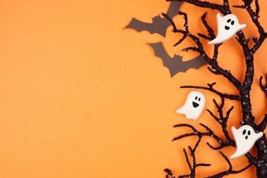 Cadılar Bayramı tarafındaki korkunç yarasalar, şeker hayaletler ve siyah dallar. Fotokopi alanı olan turuncu bir arkaplan üzerinde görünüm.