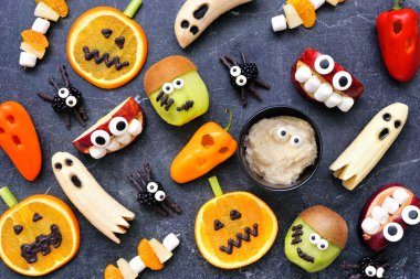 Sağlıklı Cadılar Bayramı meyveleri ve sebze atıştırmalıkları. Çeşitli eğlenceli, ürkünç şeyler. Düz bir manzaranın üzerinde koyu bir taş zemin uzanıyordu..