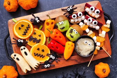 Sağlıklı Cadılar Bayramı meyvesi ve sebze tabağı. Çeşitli eğlenceli, ürkünç şeyler. Masanın üstünde koyu renkli bir arkaplan var..