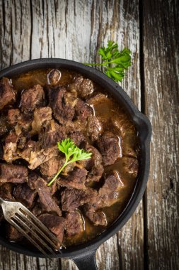 Dökme demir tavada sığır güveci, ahşap arka plan. Yüzeyin derinliği. Üst görünüm.