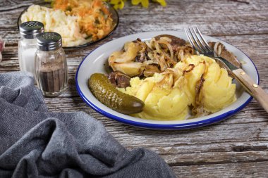 Kızarmış ciğer, soğan ve elma haşlanmış patates ve salatalık turşusuyla servis edilir..