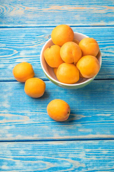 stock image Bowl full of fresh apricots on a blue wooden table.