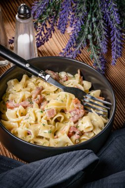 Tagliatelle Carbonara 'yı ahşap masada kasede yosunluyor. Sığ alan derinliği.