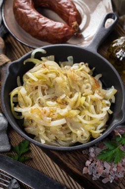 Tahta bir tezgahta duran dökme demir bir tavada kızarmış soğan..