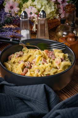 Tagliatelle Carbonara 'yı ahşap masada kasede yosunluyor. Sığ alan derinliği.