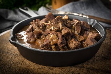 Dökme demir tavada sığır güveci, ahşap arka plan. Sığ alan derinliği.