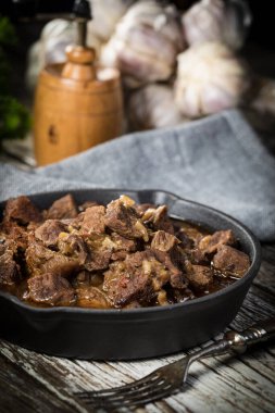 Dökme demir tavada sığır güveci, ahşap arka plan. Sığ alan derinliği.