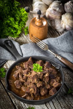 Dökme demir tavada sığır güveci, ahşap arka plan. Sığ alan derinliği.