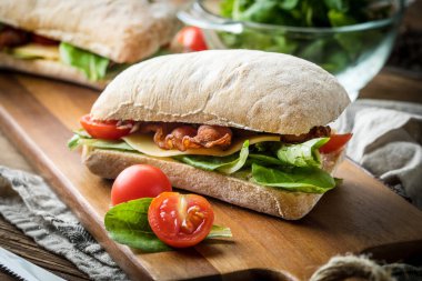 Ahşap tahta üzerinde Roka Salatası, pastırma ve sarı peynirli ciabatta sandviç.