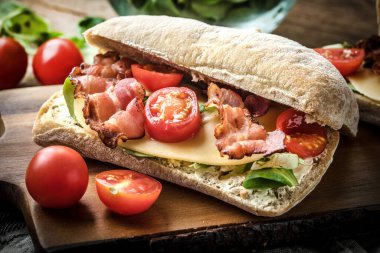 Ahşap tahta üzerinde Roka Salatası, pastırma ve sarı peynirli ciabatta sandviç.