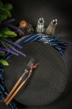 Baharatlar, otlar ve çatal bıçaklarla dolu karanlık bir arka planda boş bir siyah tabak..