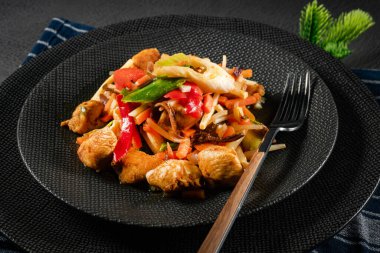 Siyah tabakta sebzeli kızarmış tavuk parçaları..