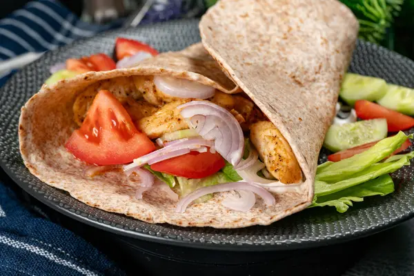 Wholegrain tortilla wraps with vegetables and chicken on a plate on the table.