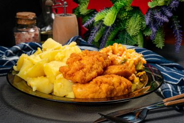 Patates ve salatayla servis edilen ekmek kırıntılarında kızarmış tavuk parçaları. Sığ alan derinliği.