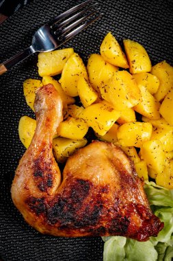Appetizing baked chicken leg quarter with browned skin served with crispy fries for dinner.