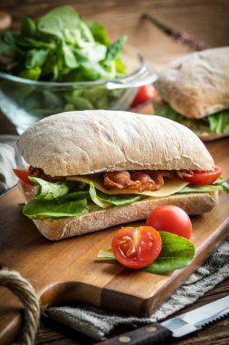 Ahşap tahta üzerinde Roka Salatası, pastırma ve sarı peynirli ciabatta sandviç.