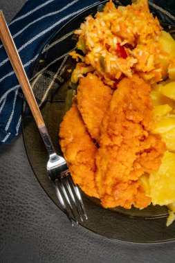 Patates ve salatayla servis edilen ekmek kırıntılarında kızarmış tavuk parçaları. Üst Manzara. Sığ alan derinliği.