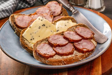 Peynirli ekmek dilimleri ve mavi tabakta sosis..