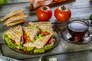 Panini sandviçle jambon, domates, marul bir plaka üzerinde.