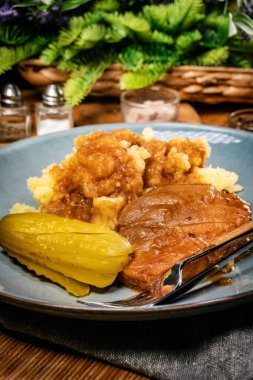 Kendi sosunda haşlanmış domuz eti patates püresi ve salatalık turşusuyla servis edilir..