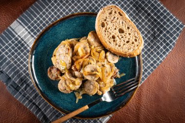 Mavi tabakta soğanla pişirilmiş beyaz sosis dilimleri. Sığ alan derinliği.