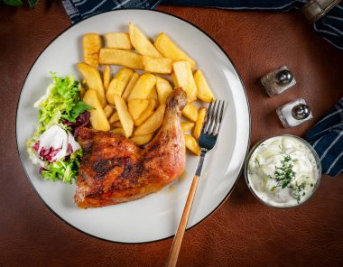 Appetizing baked chicken leg quarter with browned skin served with crispy fries for dinner.