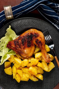 Appetizing baked chicken leg quarter with browned skin served with crispy fries for dinner.