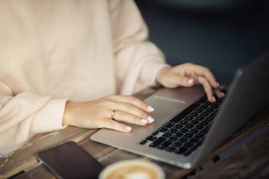 Güzel hafif manikürlü evli bir kızın elleri bir kafedeki terasta dizüstü bilgisayarda bir klavyede bir fincan kahve yazıyor. Kadın programcı bir restoranda bir program yazıyor.