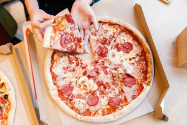 İki neşeli genç kız öğrenci bir kafede iki sıcak pizza yer zeytin, sosis, mısır ve pastırma ile.