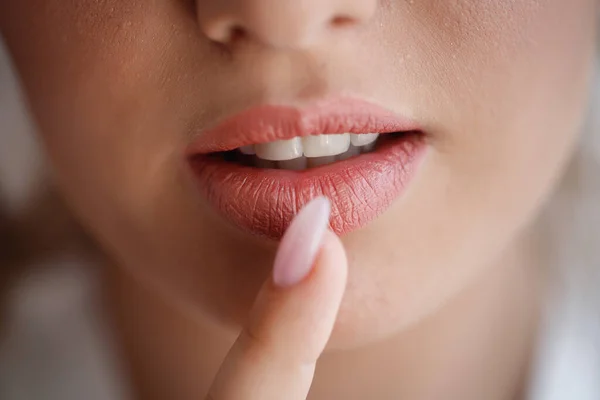 The bride girl with large magnificent lips and healthy white teeth presses a finger with a long manicure to her mouth. Very close-up, macro shot