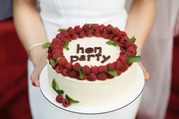 新鮮な熟したラズベリーで飾られたお祭りの白いケーキは 独身パーティーのために 白いドレスの女の子は自然のおいしいケーキを手に持っています 顔のない女性の手 — ストック写真