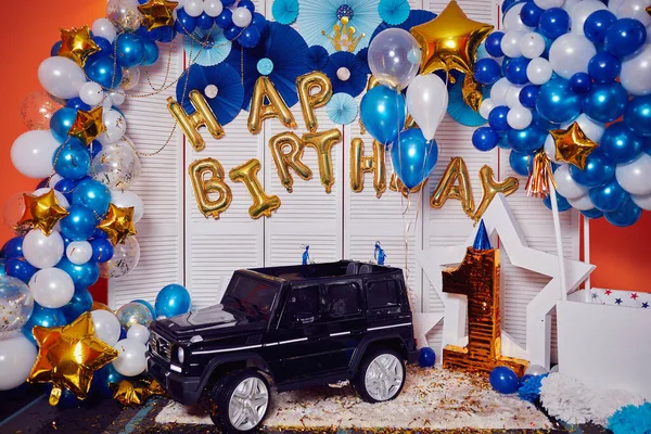 Decor of golden balloons for a little boy\'s birthday celebration. First holiday in the life of the baby. Decorated photo zone with balls, stars and sweets. Large black radio-controlled toy jeep
