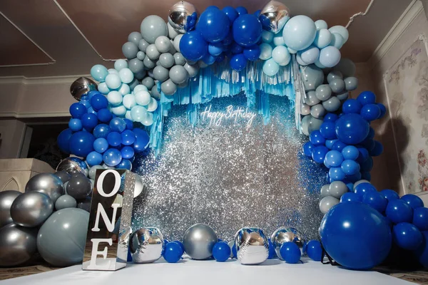 A huge photo zone for a little boy for his birthday in blue and silver colors with large inflatable balloons of different colors and the inscription one