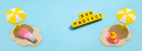 Summer skin care concept. Sunscreen, duck in inflatable ring , sand and sun umbrella on a blue background.  Text from letters on yellow cubes