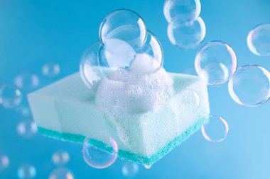 Mavi arka planda köpük ve sabun köpüğü olan açık mavi temizlik süngeri. Ev işleri ya da temizlik hizmetleri. Temizlik malzemeleri konsepti..