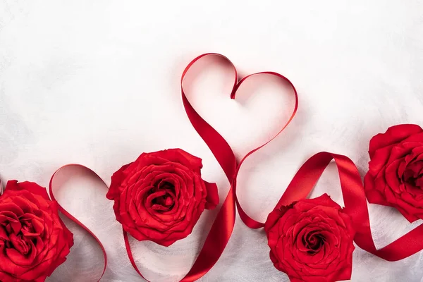 Kırmızı gül ve kırmızı kurdele vintage beyaz-gri arka plan üzerinde kalp şeklinde. Sevgililer günü için festival kavram. Kopya alanı ile üstten görünüm.