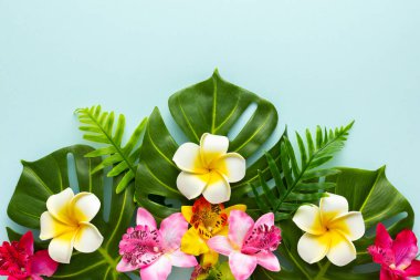 Summer background with tropical orchid flowers and green tropical palm leaves on light background. Flat lay, top view. Summer party backdrop