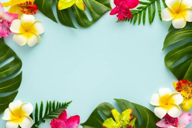 Summer background with tropical orchid flowers and green tropical palm leaves on light background. Flat lay, top view. Summer party backdrop